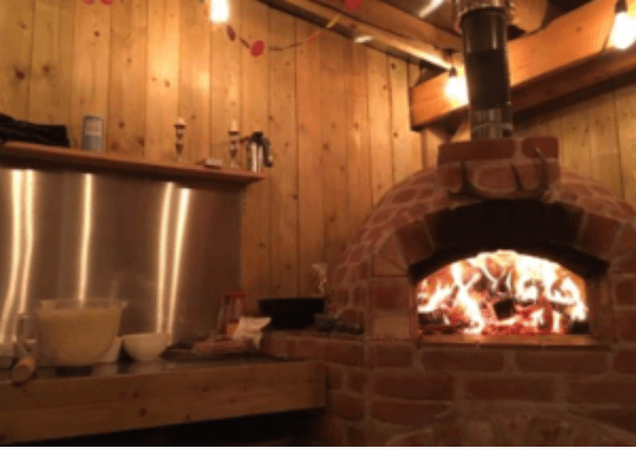 An outdoor pizza oven with fire burning inside being used as an outdoor heater for a garden.